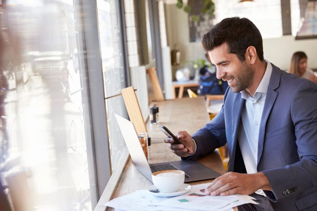 A man sitting at a table with his phone and laptop.