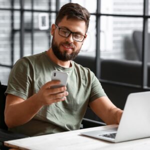 A man sitting at a table with his phone and laptop.