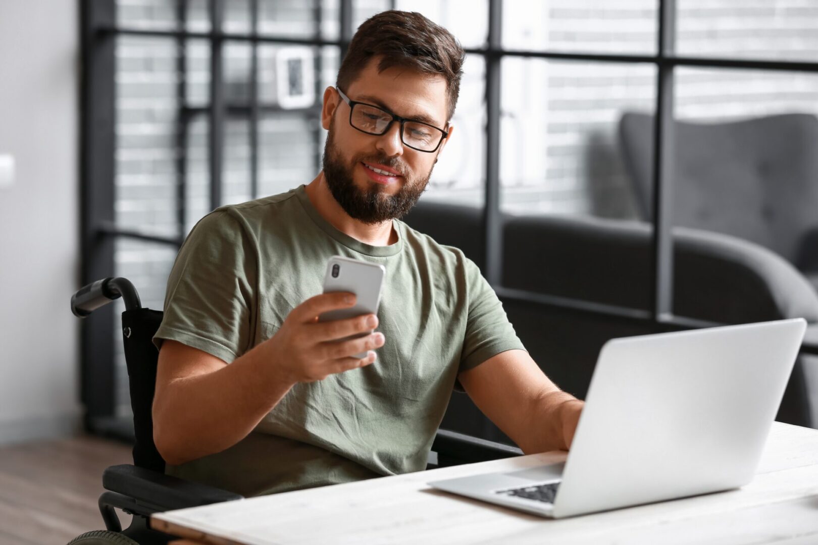 A man sitting at a table with his phone and laptop.