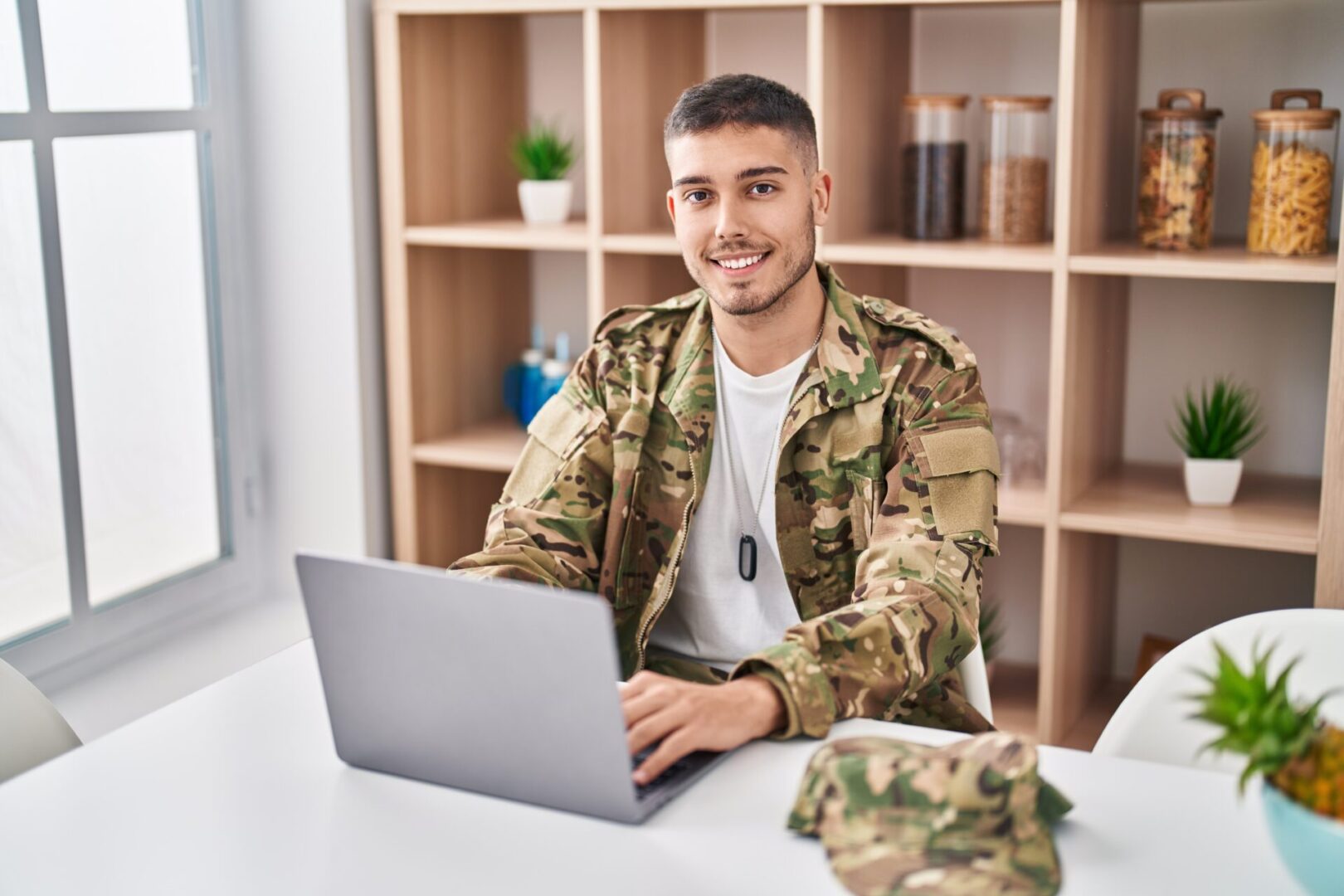 A man in camouflage uniform sitting at a table with a laptop.