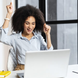 A woman sitting at her desk with her hands raised in the air.