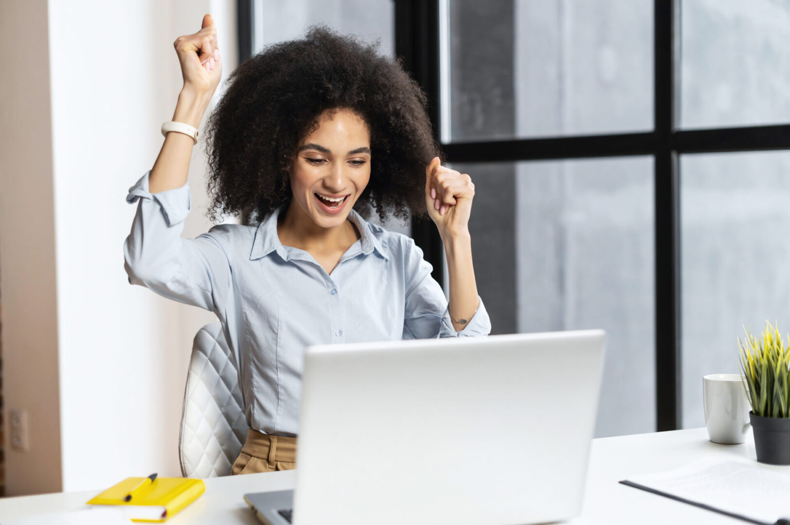 A woman sitting at her desk with her hands raised in the air.